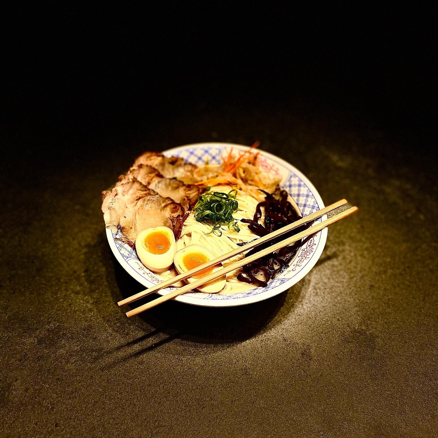 A bowl of ramen with chashu and egg, chopsticks on the rim
